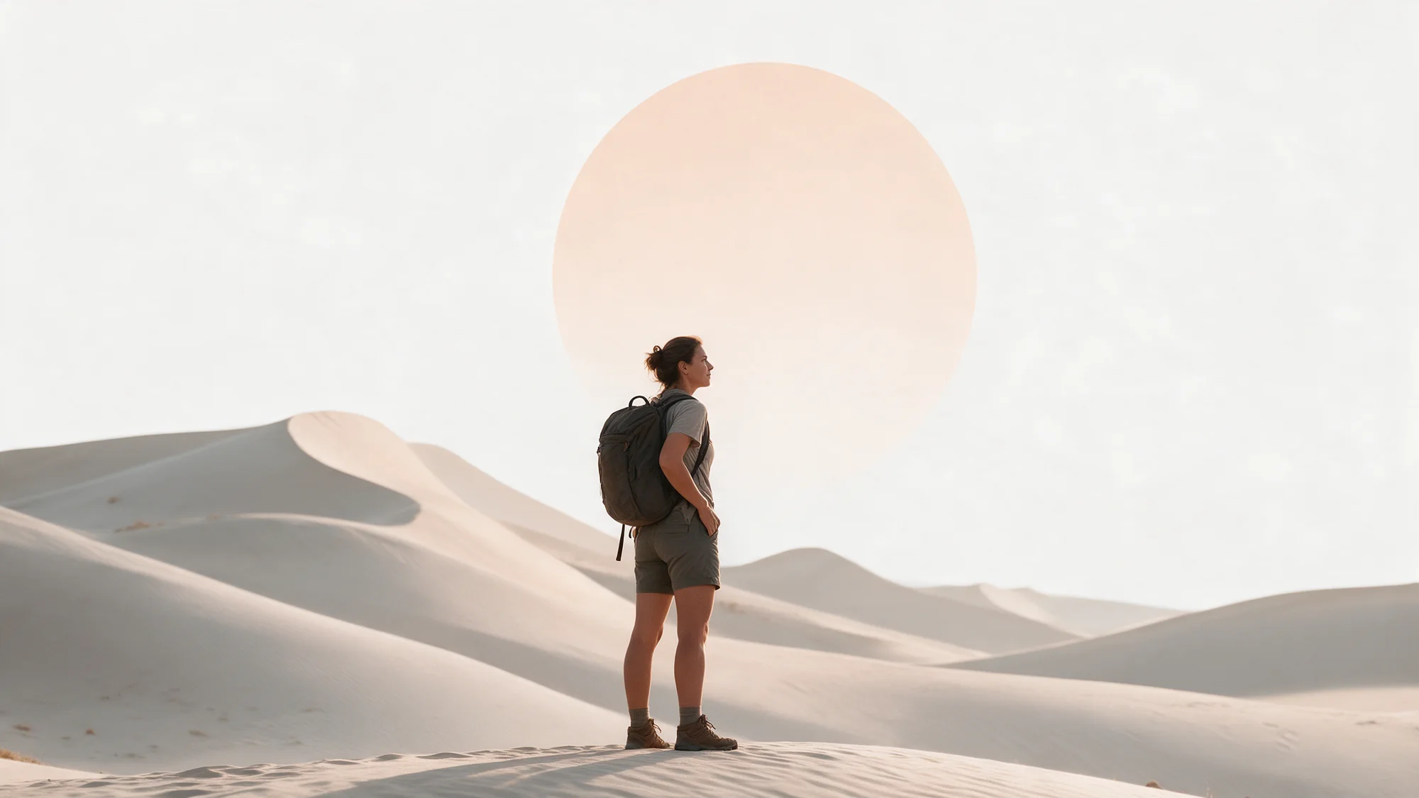 Pessoa com mochila no alto de uma duna, olhando o horizonte diante de um grande sol claro